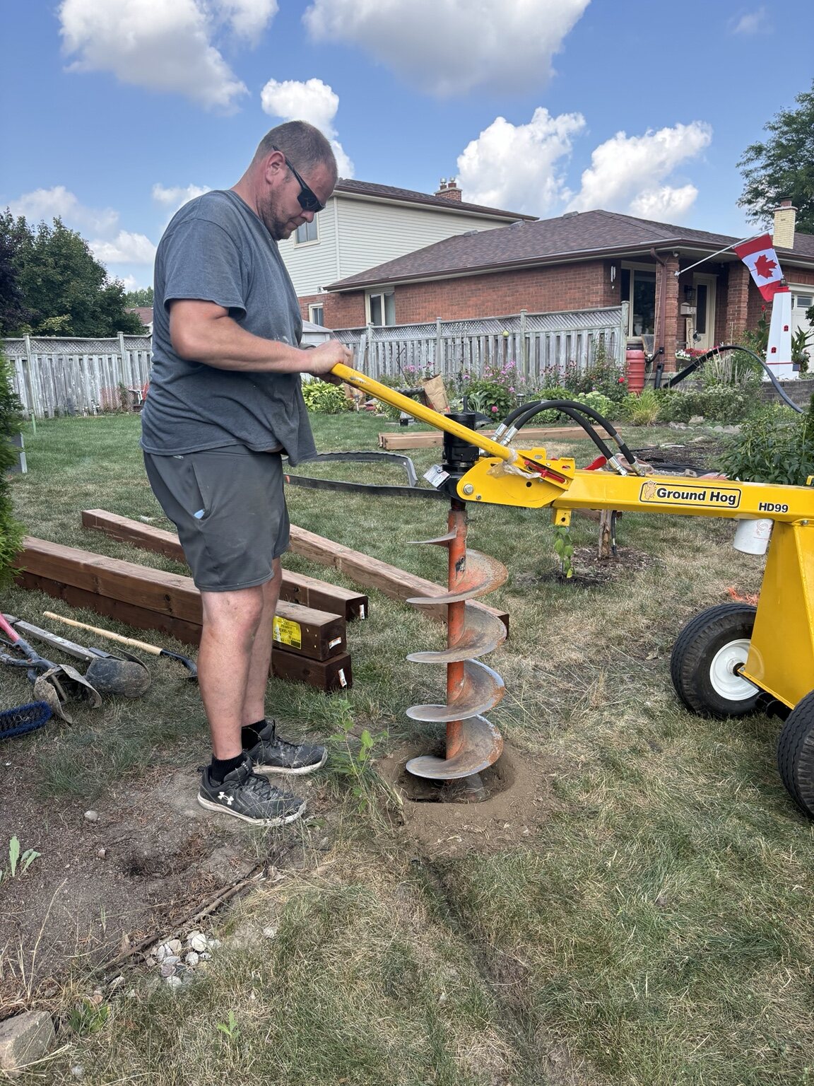 Powered auger preparing a fence-post hole in a London residential yard