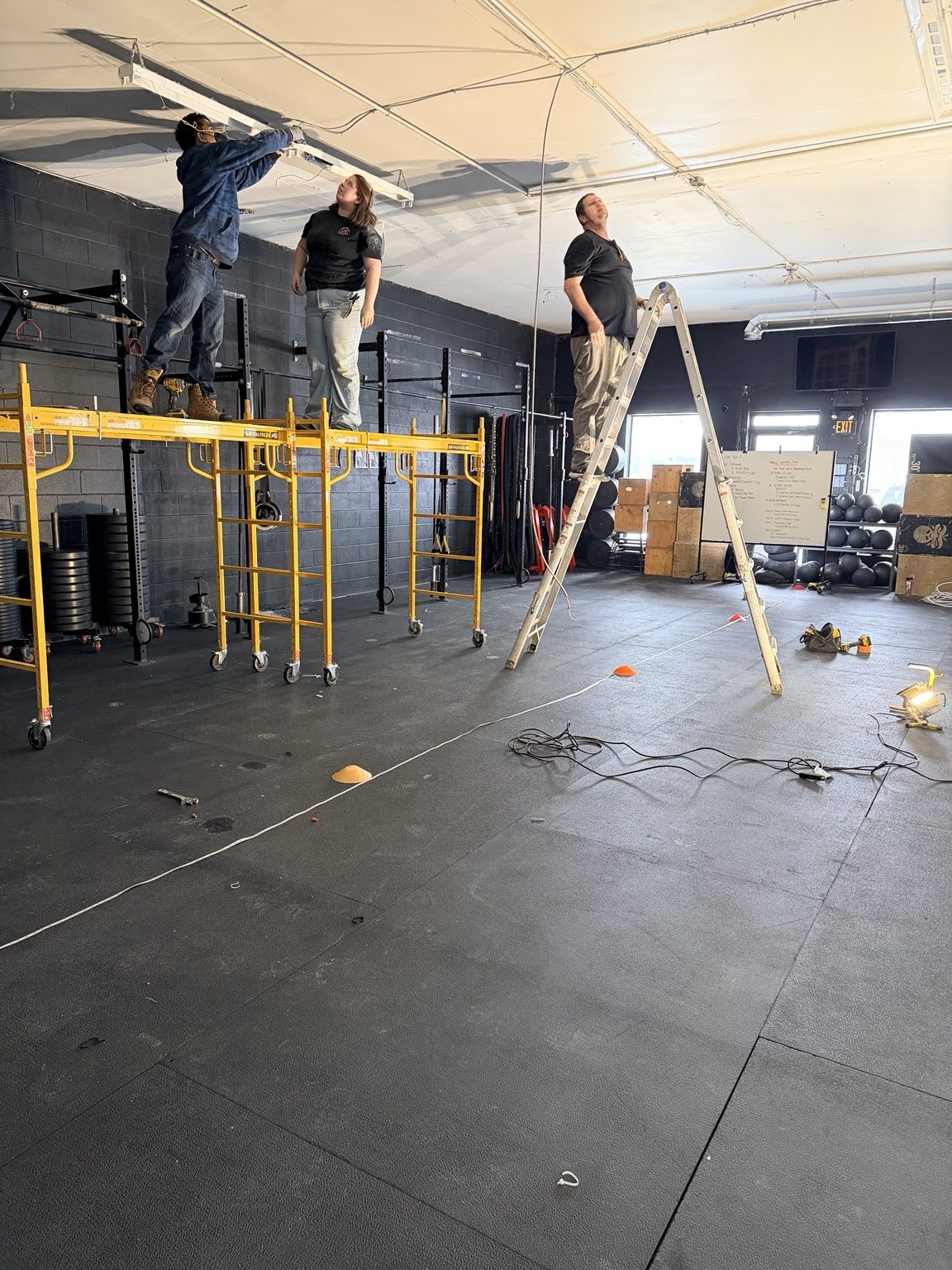 Crew replacing fitness-space lighting from scaffolding and ladders