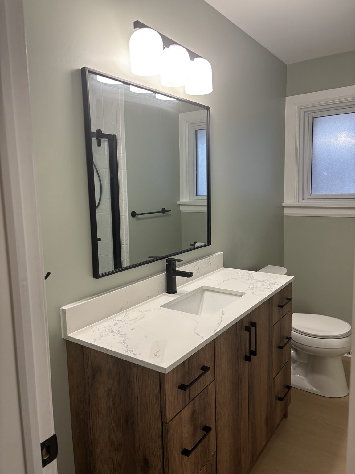 Completed bathroom with a warm wood vanity and black fixtures